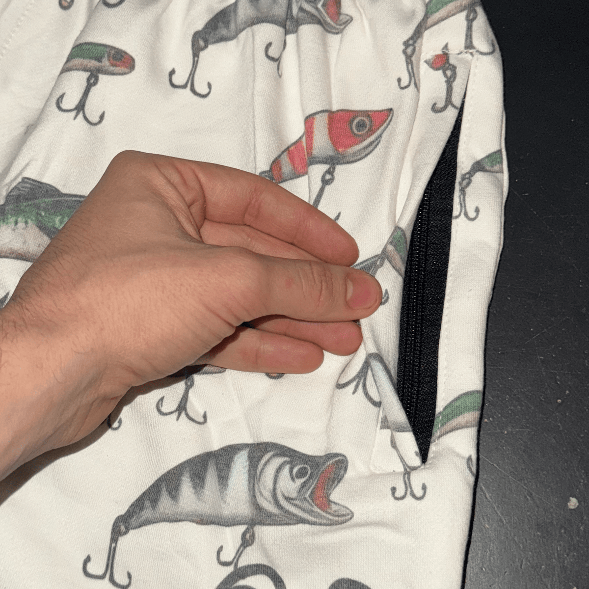Hand opening the zipper pocket on MEROX Cotton Fishing Lure shorts